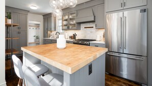 A modern kitchen with grey cabinets, a stainless steel refrigerator, a wooden island, and pendant lighting. - MINNeSTAY* Shoreline Villa | Pool (Robbinsdale)