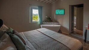 A bedroom with a large bed, a bathtub, a window with curtains, and a TV on the wall. - Borgo Elissa (Certaldo)