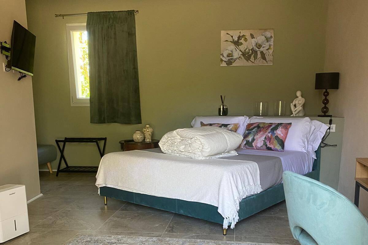 A bedroom with a bed, a chair, a TV, a window with curtains, and a painting on the wall.