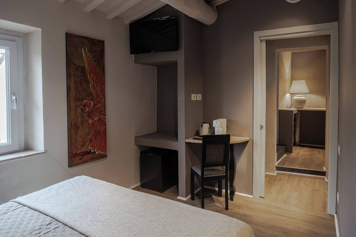 A bedroom with a bed, a desk with a chair, a TV, and a painting on the wall.