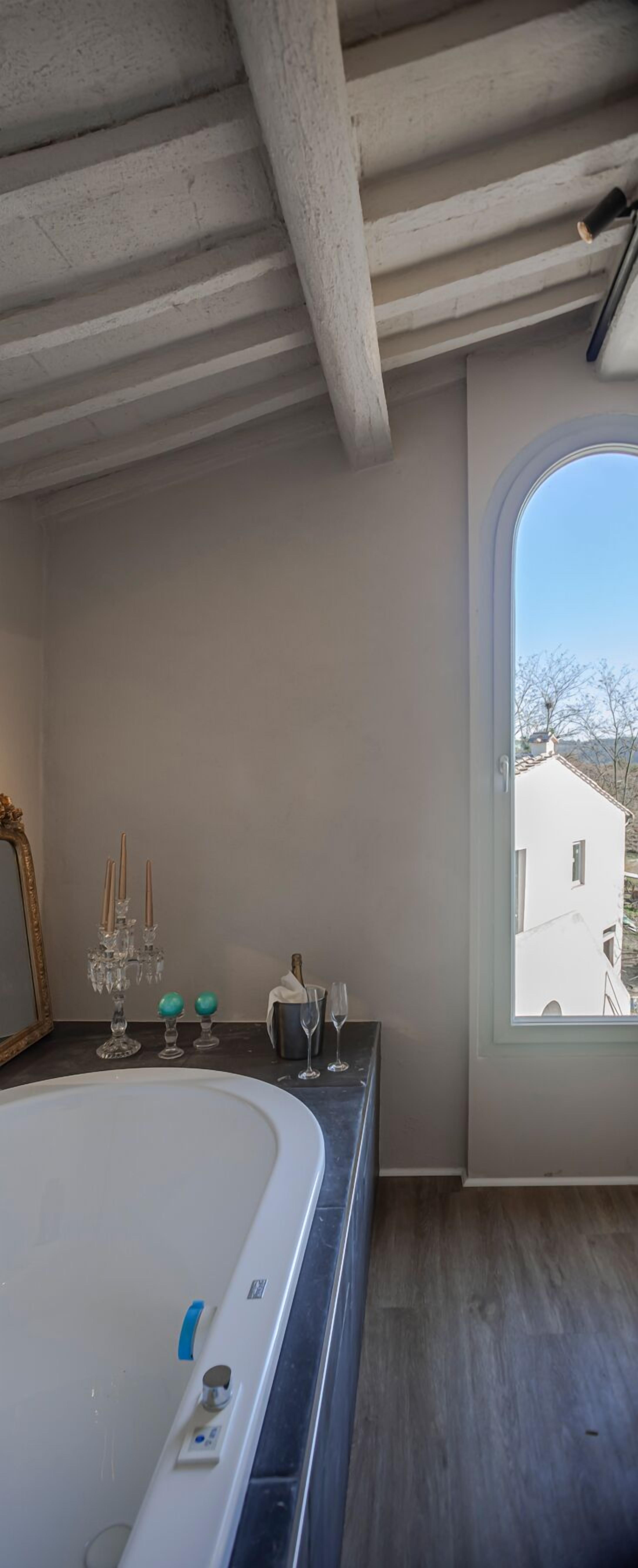 Ein Badezimmer mit einer großen Badewanne, einem Fenster mit Blick auf ein Haus und einem Spiegel mit dekorativem Rahmen.