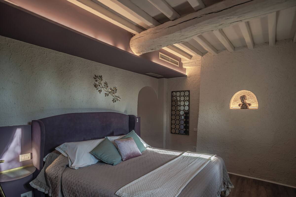 A bedroom with a large bed, a headboard, a wall-mounted light, and a decorative mirror.