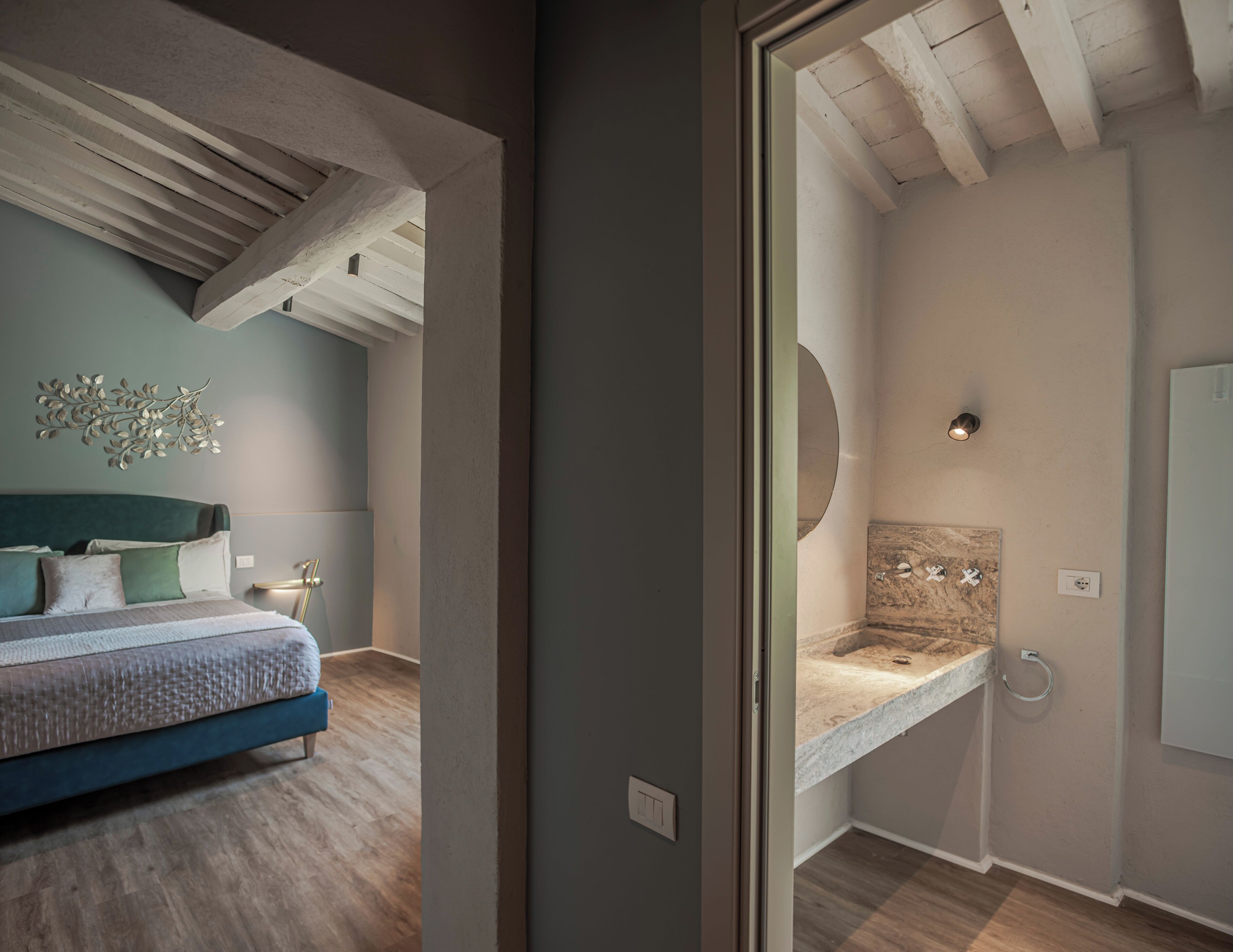A bedroom with a bed, a nightstand, a wall-mounted light, and a ceiling with exposed beams.
