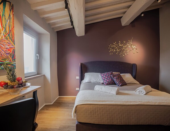 A bedroom with a bed, a desk with fruit, a window, and a ceiling with exposed beams. - Borgo Elissa (Certaldo)