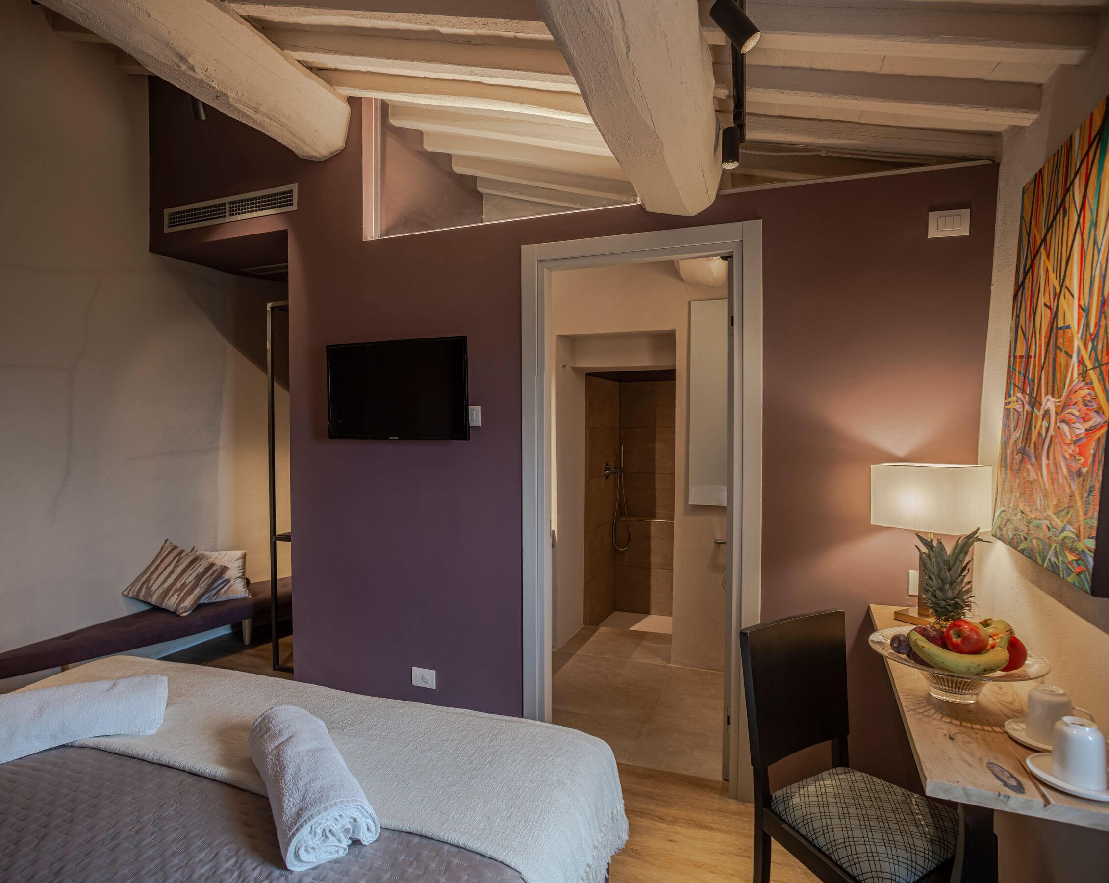 Une chambre d’hôtel avec un lit, un téléviseur fixé au mur, un espace douche et une table à manger avec des fruits, dont un ananas.