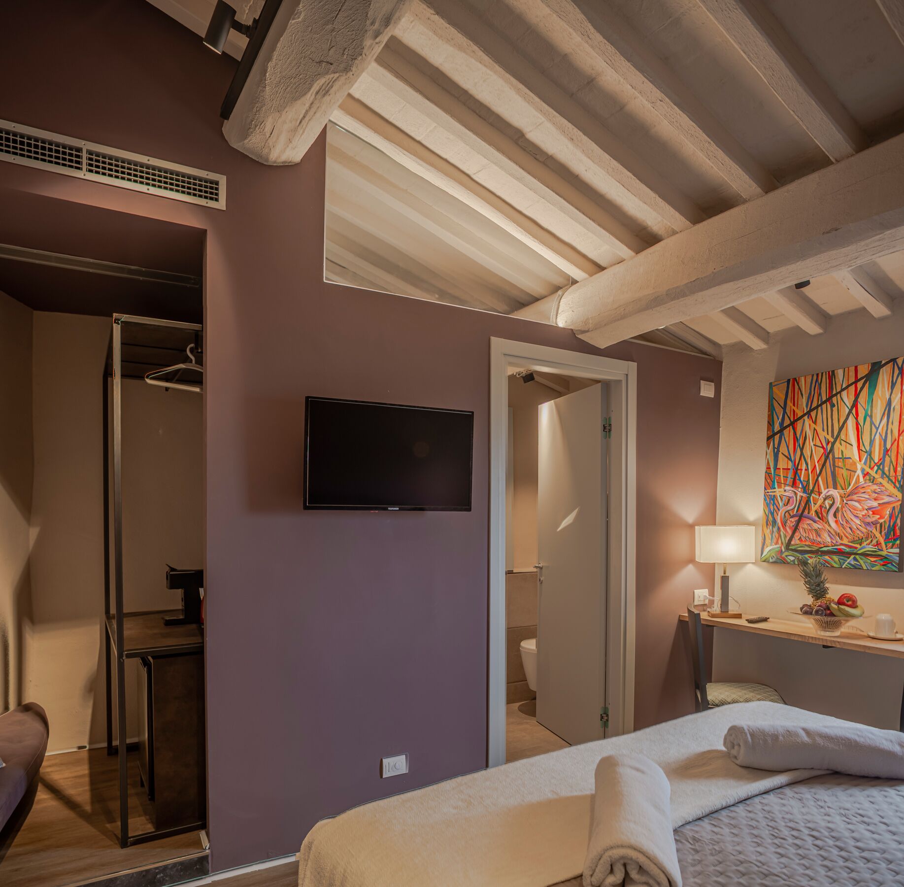 Una habitació d'hotel amb un llit, una televisió, un quadre i un bany visible a través d'una porta oberta.