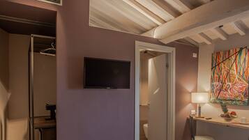 Una habitació d'hotel amb un llit, una televisió, un quadre i un bany visible a través d'una porta oberta.
