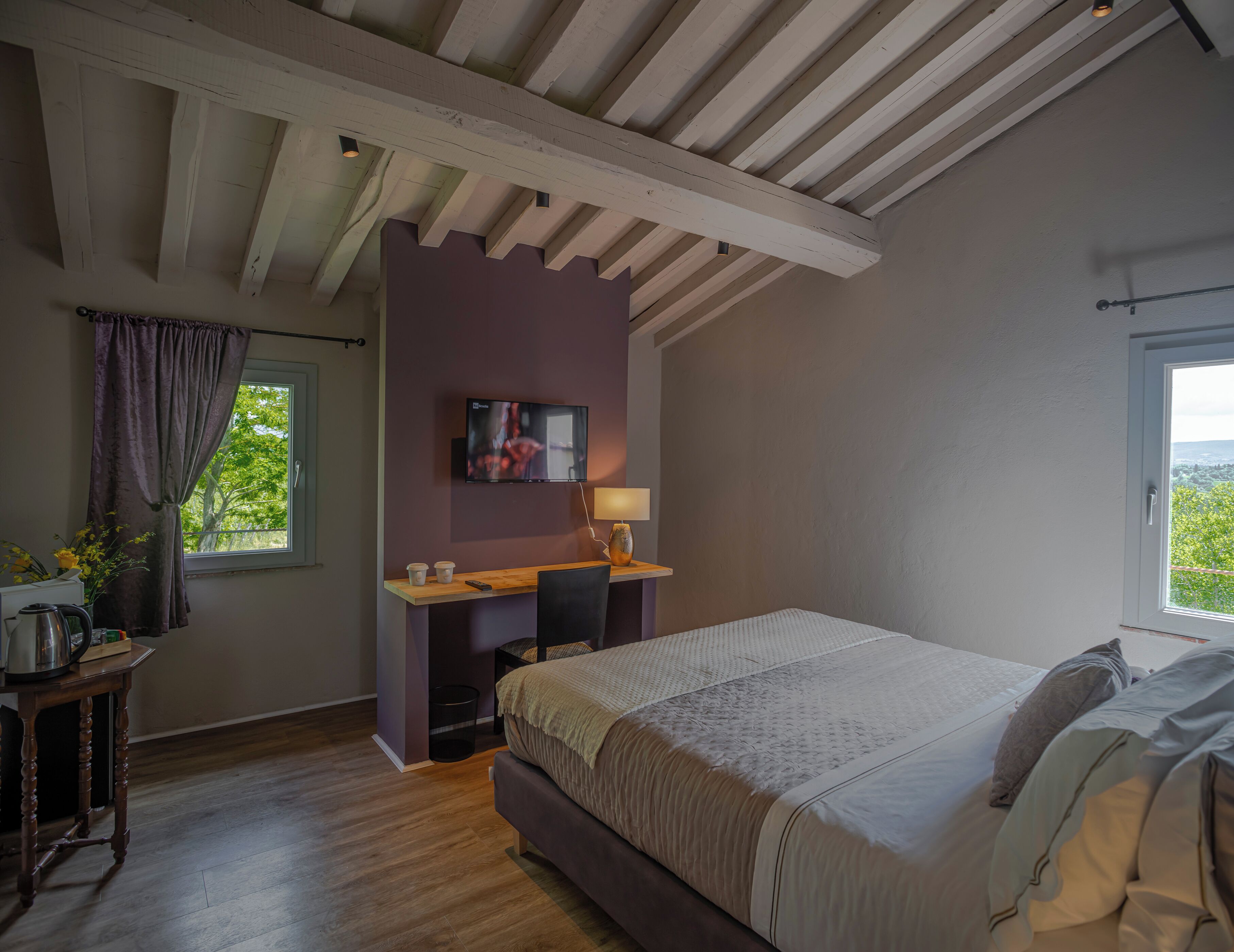 Une chambre à coucher avec un lit, un bureau, une télévision et une fenêtre avec des rideaux.