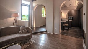 A modern living room with a sofa, a lamp, and a view through an archway to a kitchen area. - Borgo Elissa (Certaldo)