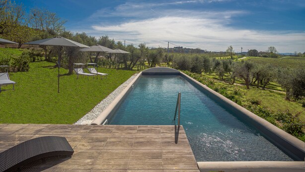 A swimming pool with a wooden deck, lounge chairs, and umbrellas in a landscaped garden. - Borgo Elissa (Certaldo)