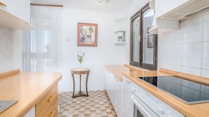 Een gezellige, kleine keuken met een geruite vloer, houten aanrecht, een klein rond tafeltje met een vaas en een lijst met een foto aan de muur.