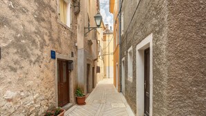 Une ruelle étroite aux murs de pierre, avec une porte en bois et des plantes en pot.