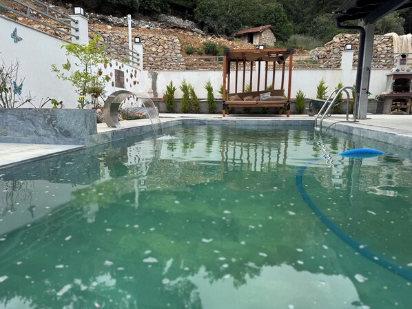 Una piscina con un banco de madera y un muro de piedra con plantas.