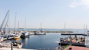 Un port de plaisance où sont amarrés différents bateaux, un petit bateau amarré avec un drapeau, et un bâtiment doté d’une terrasse.