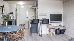 Un espace de vie compact comprenant un coin repas, une kitchenette et un téléviseur fixé au mur.