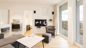 A modern living room with a flat-screen TV, comfortable seating, a dining table, and a large window offering a city view. - Awesome Apartment in Lübeck Travemünde With 3 Bedrooms, Sauna and Wifi (Lübeck)