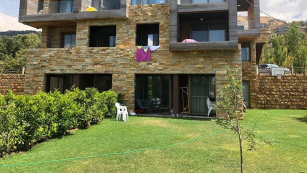 Un edificio moderno de varios pisos con fachada de piedra, ventanas amplias y un balcón visible.