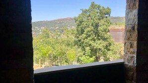 Una habitación con pared de piedra y ventana con vistas a un paisaje verde con árboles y colinas.