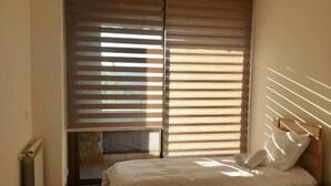 Un dormitorio con dos camas, persianas de madera, un radiador y una ventana.