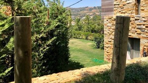 Un edificio de piedra con una valla de madera y vistas a un campo verde y colinas al fondo.