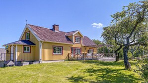 A yellow house with a red roof, a wooden deck, and a large tree in the yard. - Beautiful Home in Varberg With Wifi and 4 Bedrooms (Varberg)
