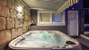 Uma área de spa com paredes de pedra, uma banheira de hidromassagem, uma janela e uma porta.