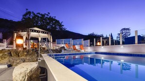 Piscina com borda de pedra, área de estar coberta com cadeiras laranja e lareira.