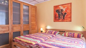 Un dormitorio con una cama grande, una mesita de noche con lámpara, un armario de madera y un cuadro en la pared.