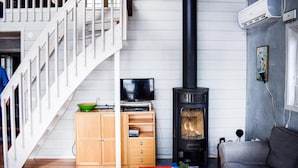 A cozy living room with a wooden staircase, a TV, a bookshelf, and a wood-burning stove. - Nice Home in Hyltebruk With 3 Bedrooms, Sauna and Wifi (Hyltebruk)