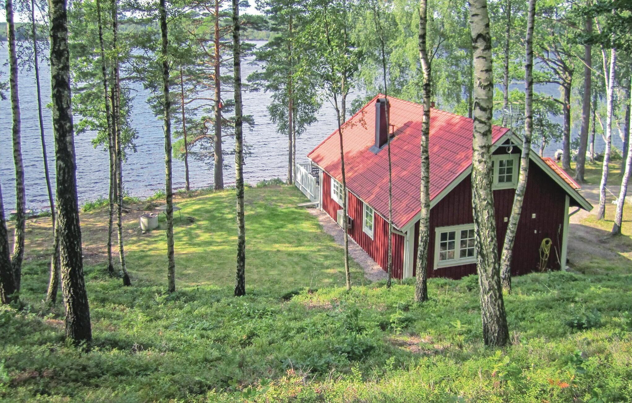 A red cabin with a red roof, surrounded by trees and a lake.