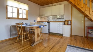 Una cocina con piso de madera, una mesa de comedor con sillas, un refrigerador y una escalera de madera.