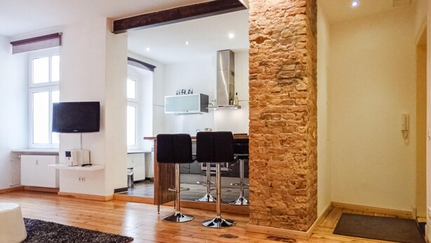 A modern living room with a stone accent wall, a flat-screen TV, and a dining area with bar stools. - Beautiful Apartment in Berlin With 1 Bedrooms and Wifi (Berlin)