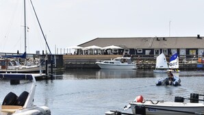 A marina with boats, a sailboat with a blue and white flag, and a building with outdoor seating. - Awesome Apartment in Ystad With (Ystad)