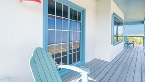 Ein überdachter Balkon mit blauem Stuhl, einer roten Pendelleuchte und Blick auf den Ozean.
