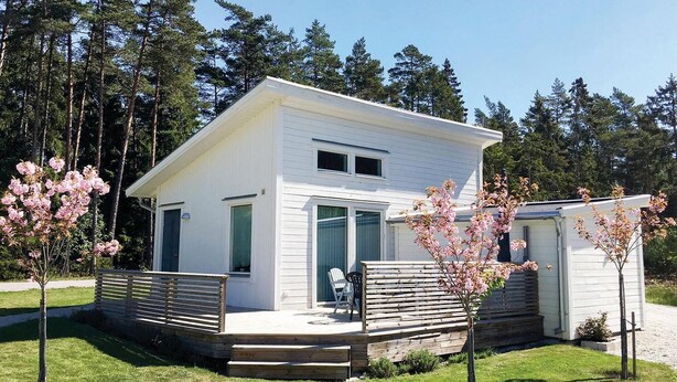 A modern white two-story house with a deck, surrounded by trees and a well-maintained lawn. - Amazing Home in Gotlands Tofta With 2 Bedrooms (Gotlands Tofta)