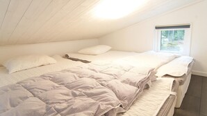 A bedroom with a sloped ceiling, a window with a view of greenery, and a bed with multiple pillows and a striped blanket. - Amazing Home in Gotlands Tofta With 2 Bedrooms (Gotlands Tofta)