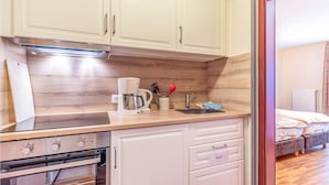 A compact kitchen with white cabinets, a built-in oven, a coffee maker, and a sink. - Hotel Wittensee (Gross Wittensee)