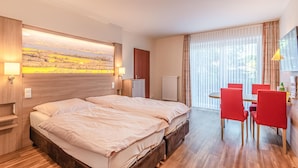 A hotel room with a double bed, a small desk with a chair, a radiator, and a large window with curtains. - Hotel Wittensee (Gross Wittensee)