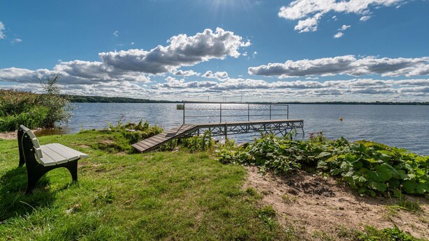 A lakeside view with a wooden dock, a bench, and a grassy area. - Hotel Wittensee (Gross Wittensee)