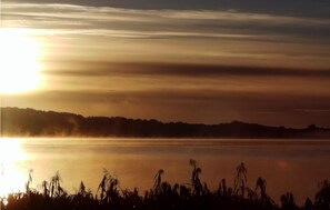 Un atardecer sobre un lago tranquilo con la silueta de árboles a lo lejos.