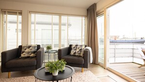 A modern living room with two sofas, a small round table with a plant, and a view of a marina through large windows. - Aqualiving (Aalsmeer)