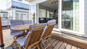 A deck with a wooden table and chairs, a sliding glass door leading to an interior space, and a view of the water outside. - Aqualiving (Aalsmeer)