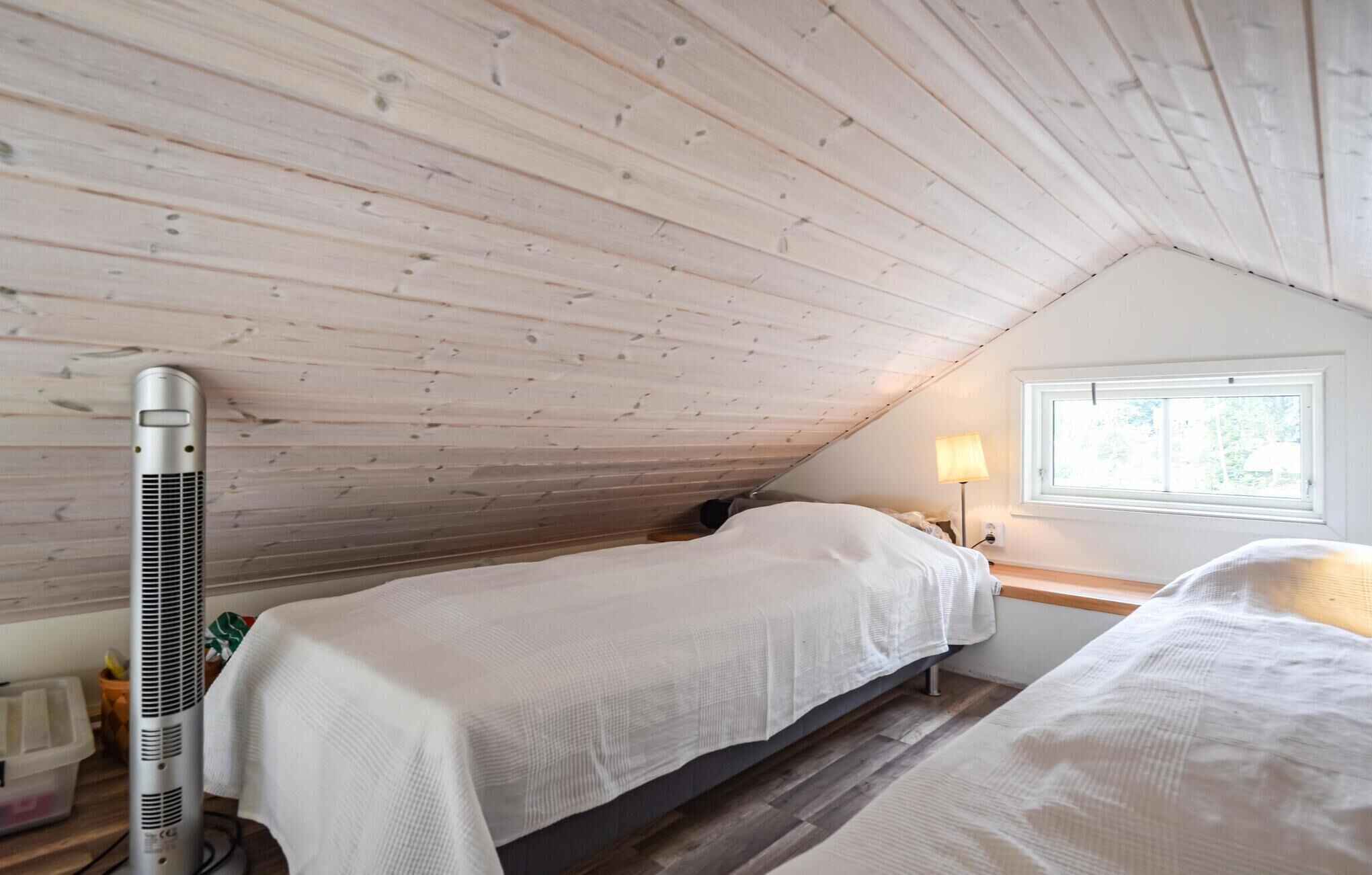 A small, cozy attic bedroom with two single beds, a heater, and a window providing natural light.