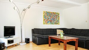 A living room with a dark grey sofa, a wooden coffee table, a floor lamp, a TV on a white stand, and a colorful abstract painting on the wall. - Awesome Apartment in Otterndorf With 2 Bedrooms and Wifi (Otterndorf)
