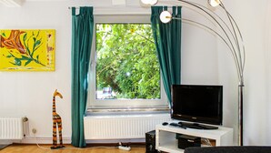 A room with a large window, a television on a white stand, a radiator, and a floor lamp. - Awesome Apartment in Otterndorf With 2 Bedrooms and Wifi (Otterndorf)