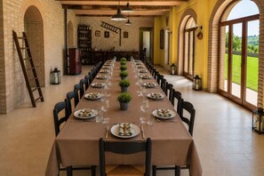 Una llarga taula de menjador preparada per a un àpat, amb caires, una prestatgeria de vi i vista a l'exterior.