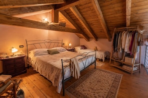 A cozy attic bedroom with two beds, wooden beams, a clothing rack, and a small table with a lamp.