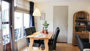 Un comedor con una mesa de madera, sillas tapizadas negras, una planta en maceta y una estantería.