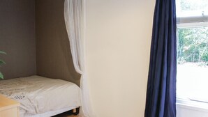 Un dormitorio con una cama individual, una ventana con cortina oscura y una planta en la esquina.