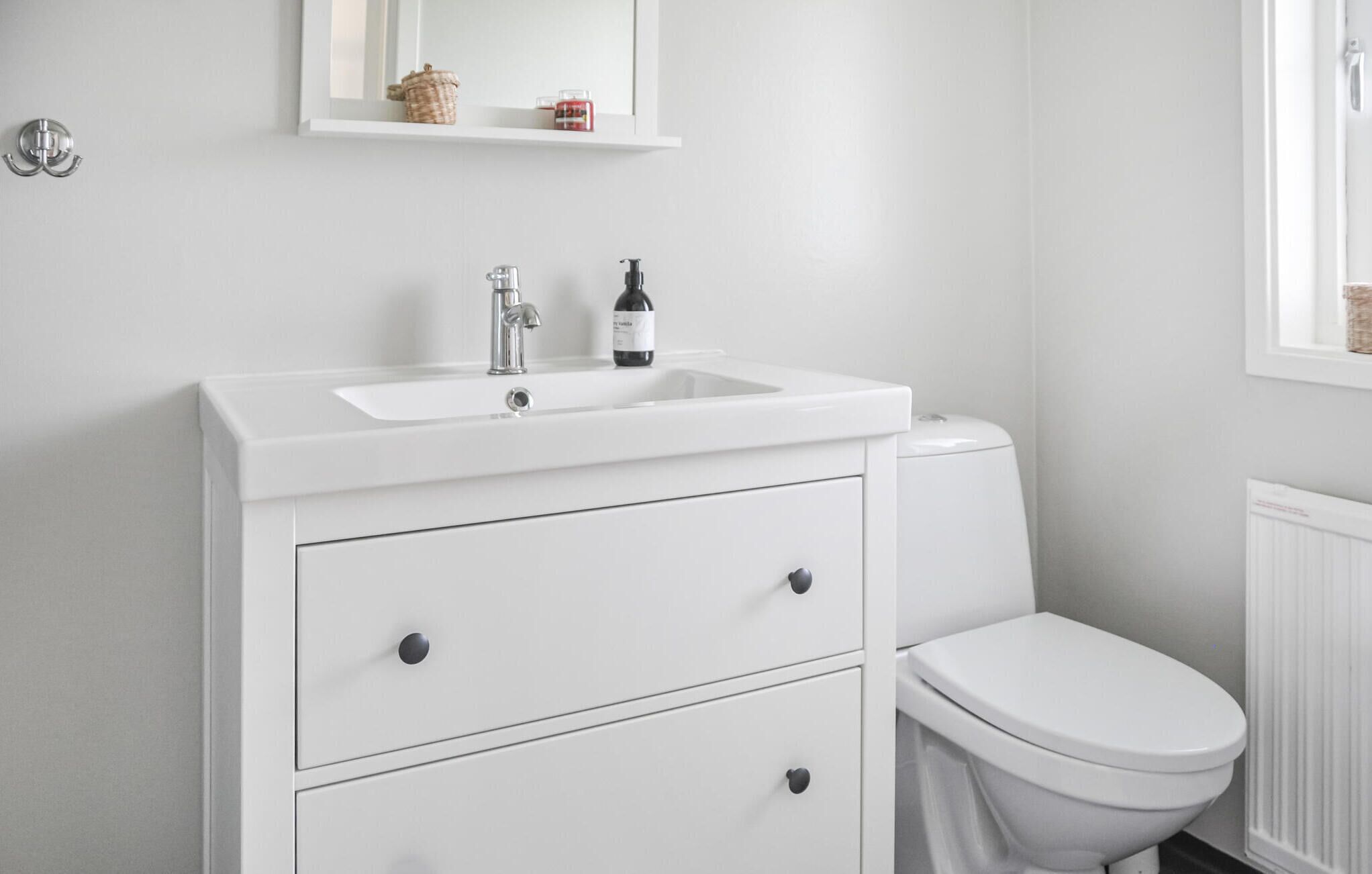 A modern bathroom with a white sink, two drawers, a toilet, and a mirror above the sink.